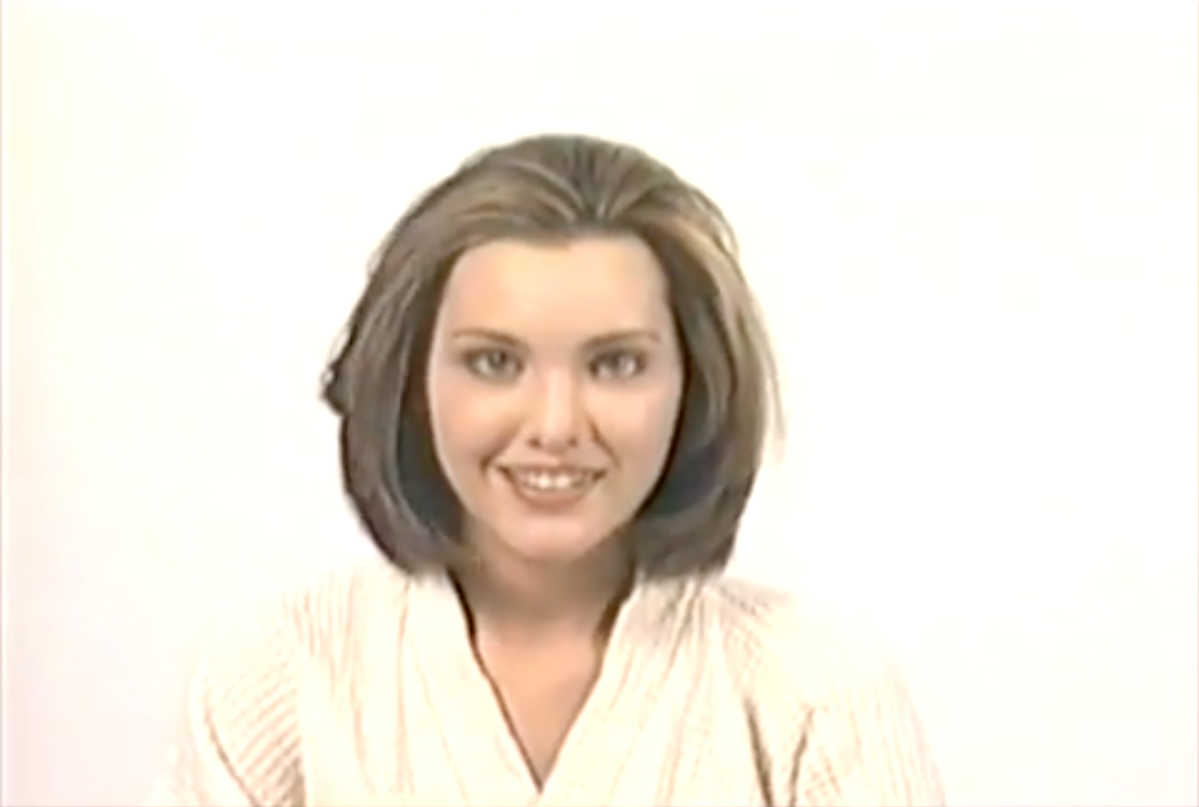 A woman in a white robe is smiling and looking at the camera.