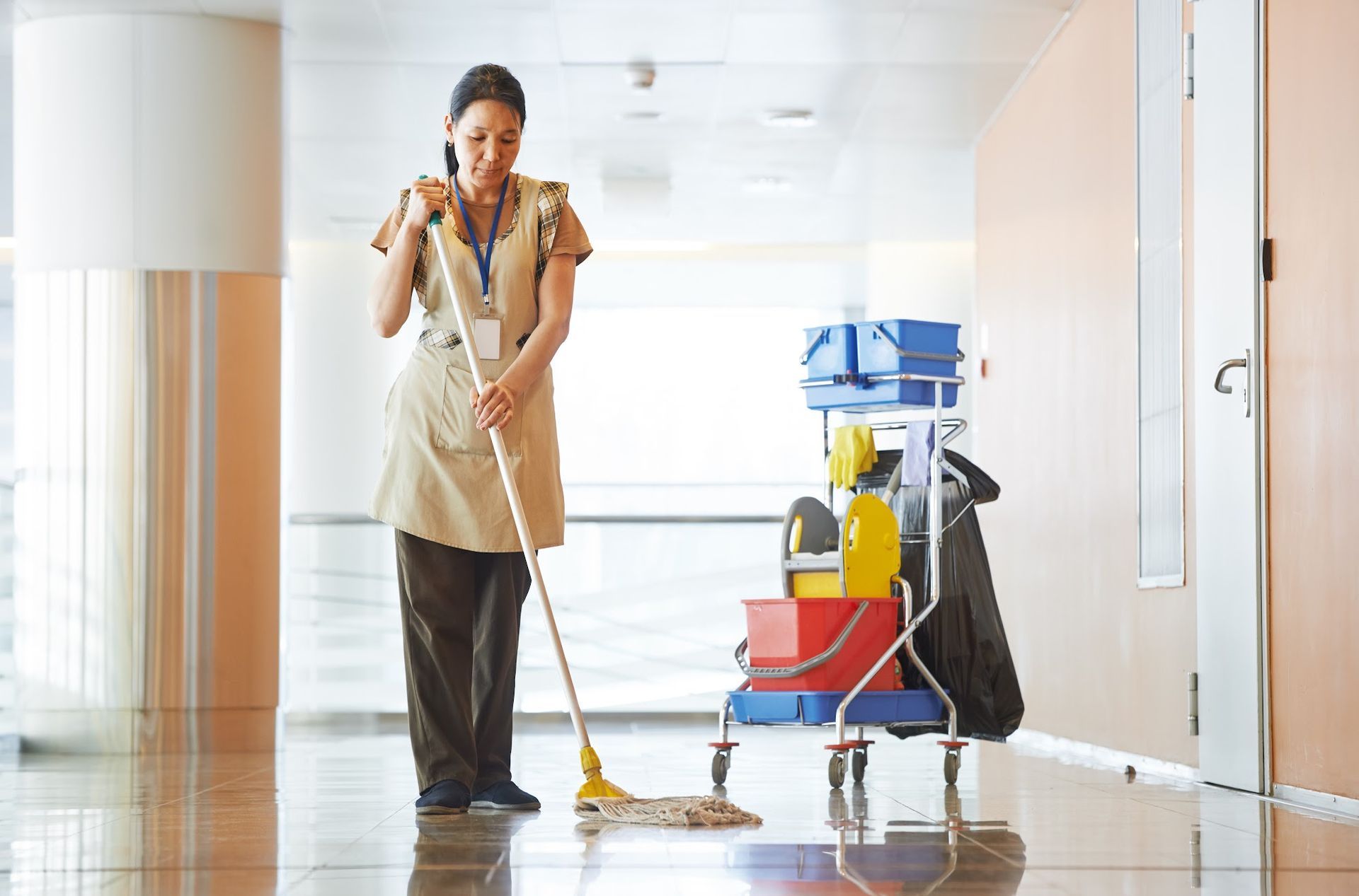 Janitor mopping a shiny hallway floor beside a cleaning cart and bucket