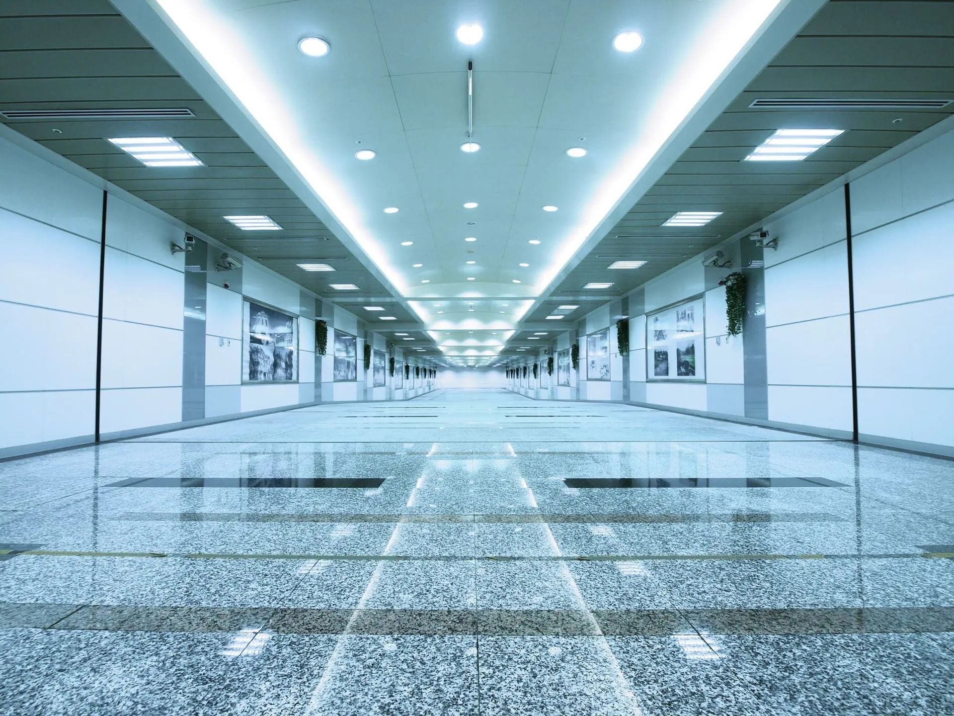 Long, light-blue tiled hallway, with recessed lighting. The walls have framed artwork.