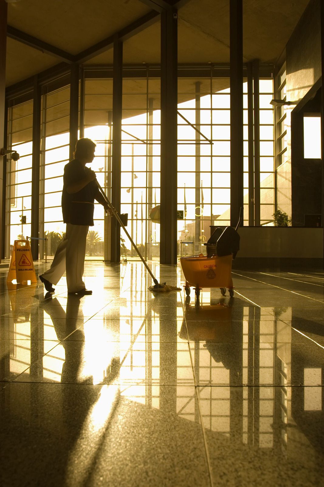 Silhouette of a person pushing a cart in a sunlit airport terminal with reflections on the floor