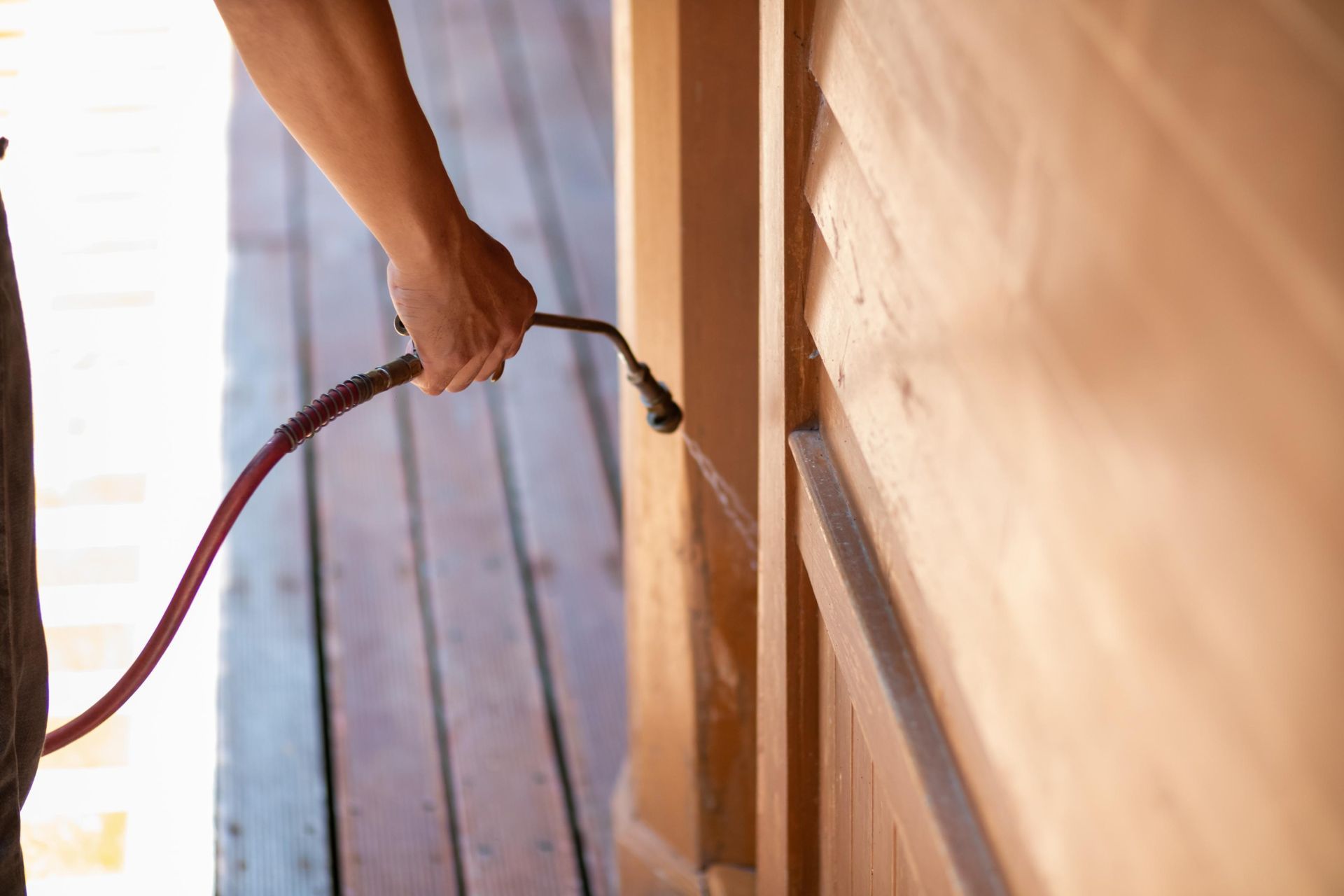 Pest control technician spraying insecticide near a piece of furniture's legs on a light-colored floor.