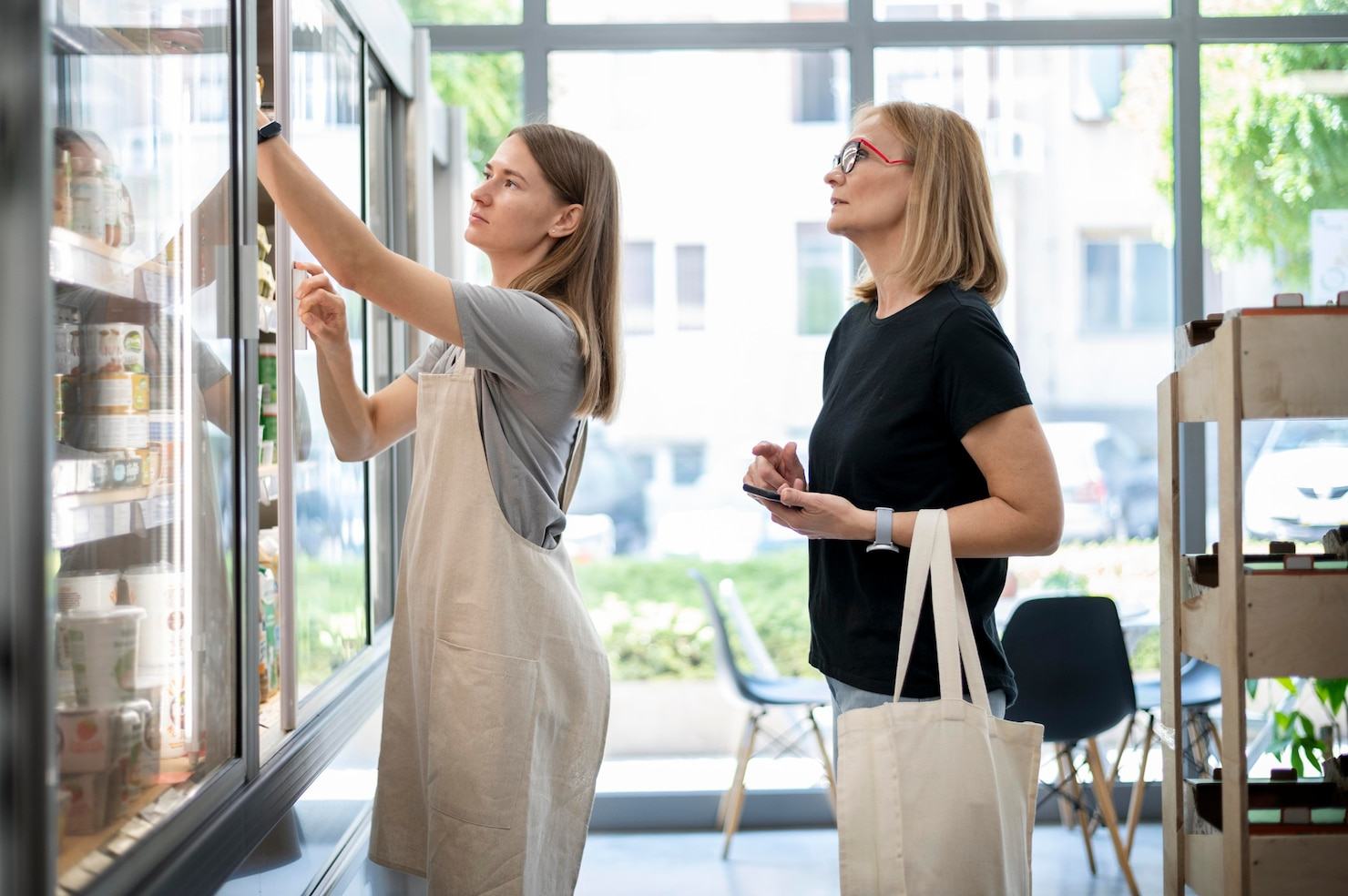 Two women are standing in front of a refrigerator in a store.