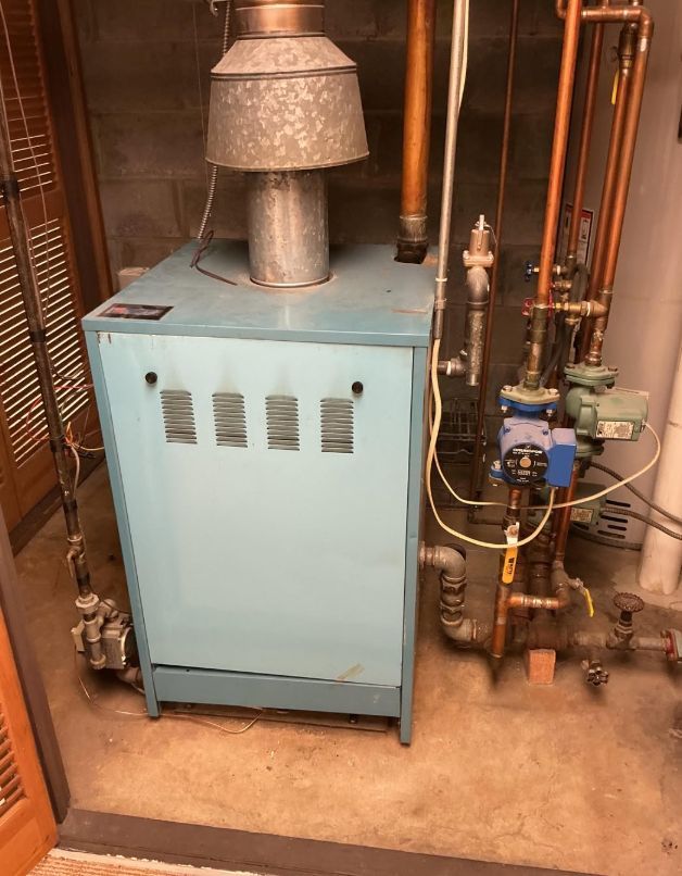 Blue furnace in a utility closet with exposed pipes and a vent pipe on top