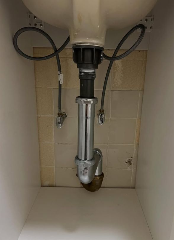 Under-sink plumbing with a chrome drain pipe and P-trap in a beige tiled cabinet