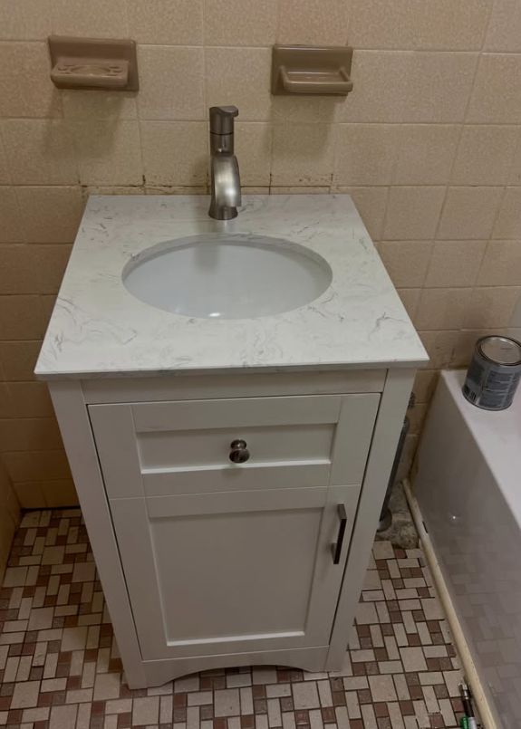 Small bathroom vanity with white sink and cabinet beside a tub, against beige tiled walls.
