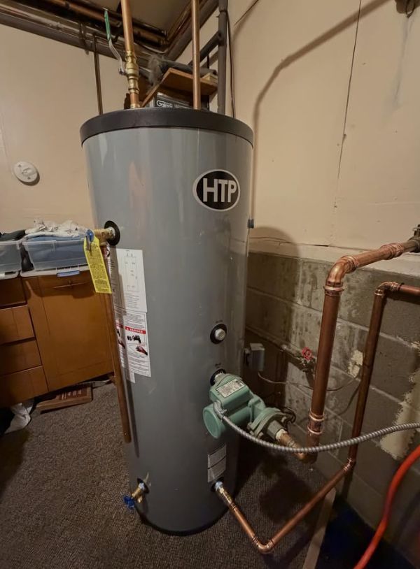 Gray water heater in a basement with copper pipes and a green circulator pump.