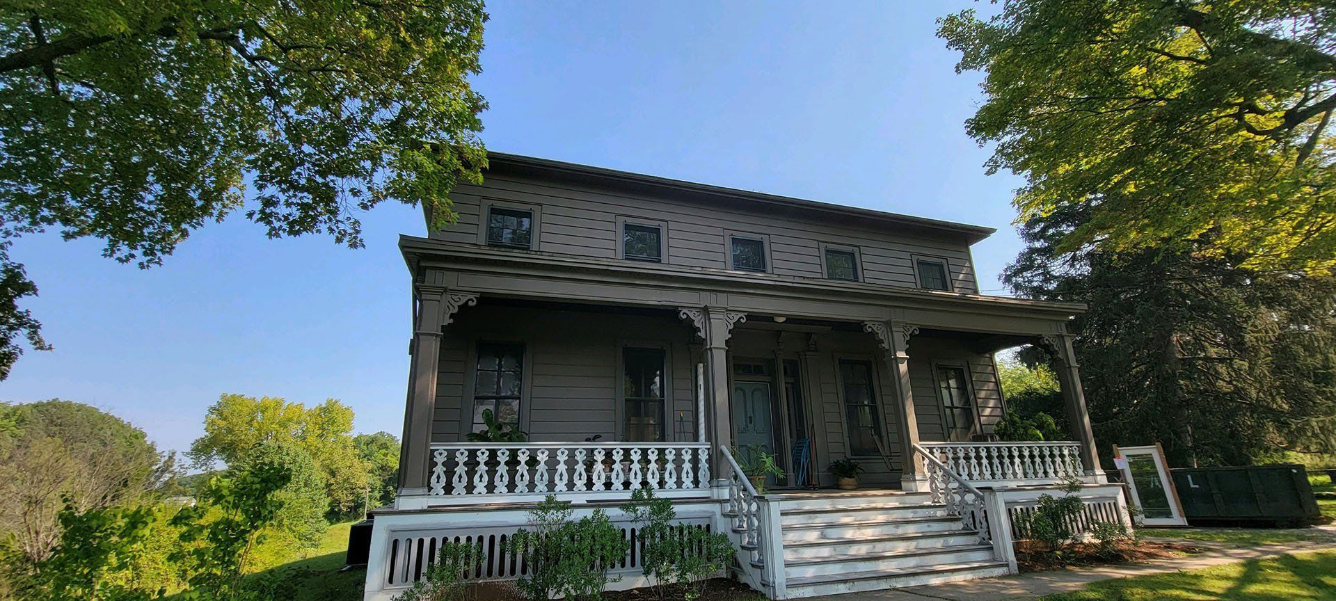 A large house with a porch and stairs is surrounded by trees.