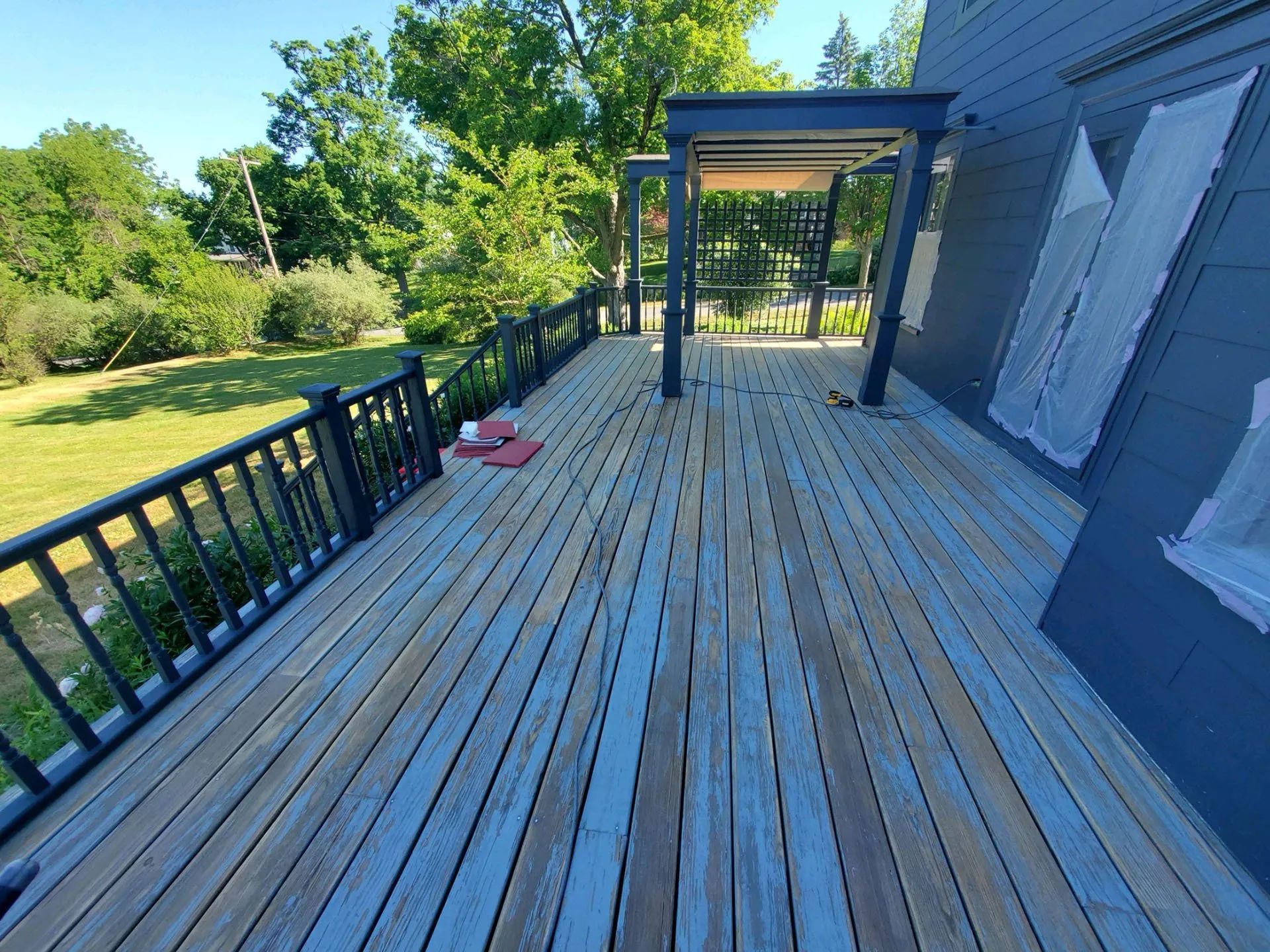 A large wooden deck with a black railing is being painted blue.