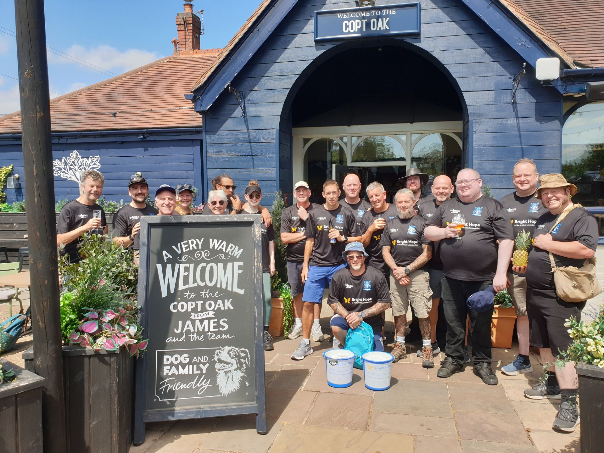Group of people in front of a pub holding drinks and a sign that says
