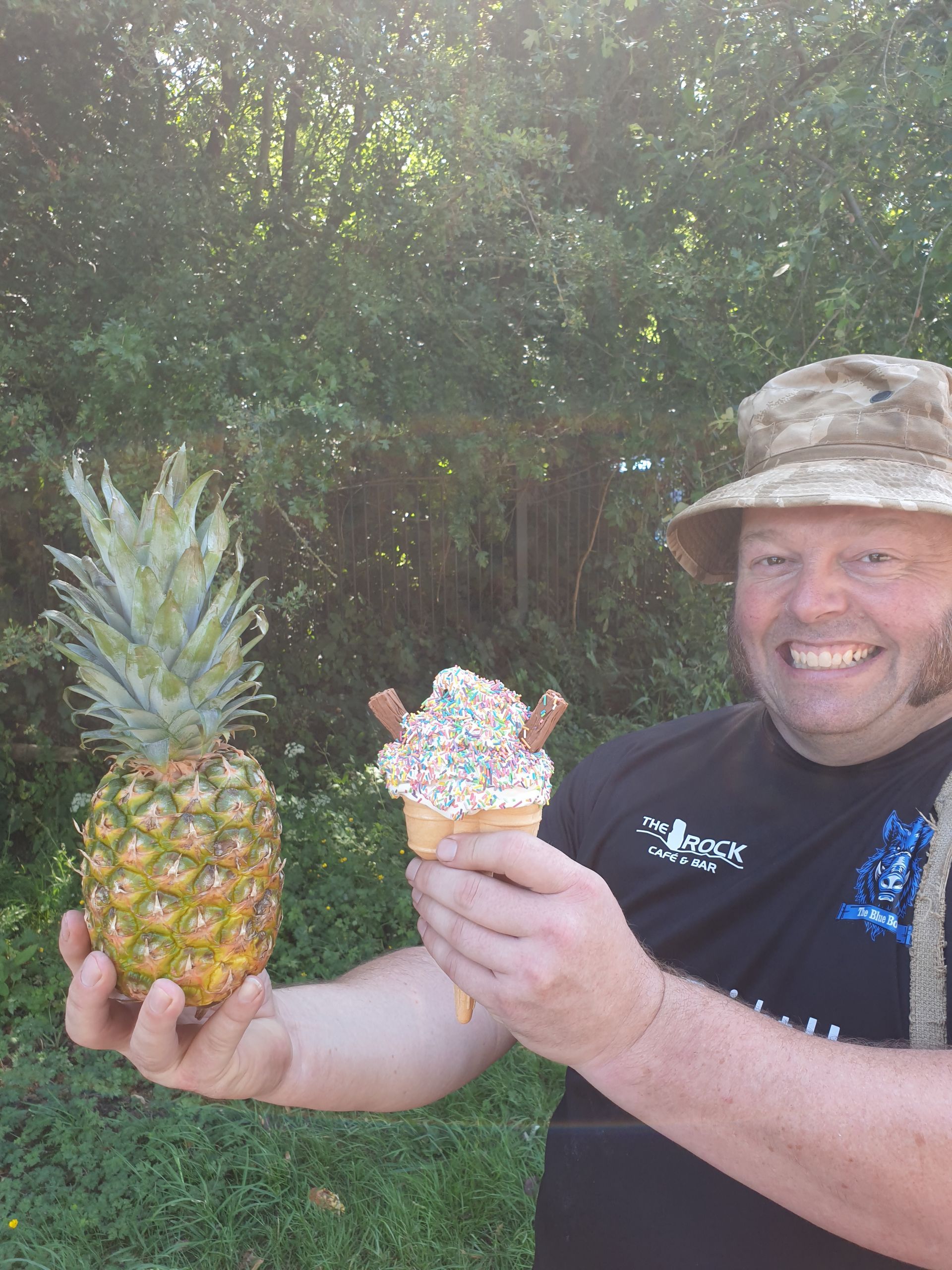 Man holding a pineapple and an ice cream cone with sprinkles and candy in front of a green backdrop.