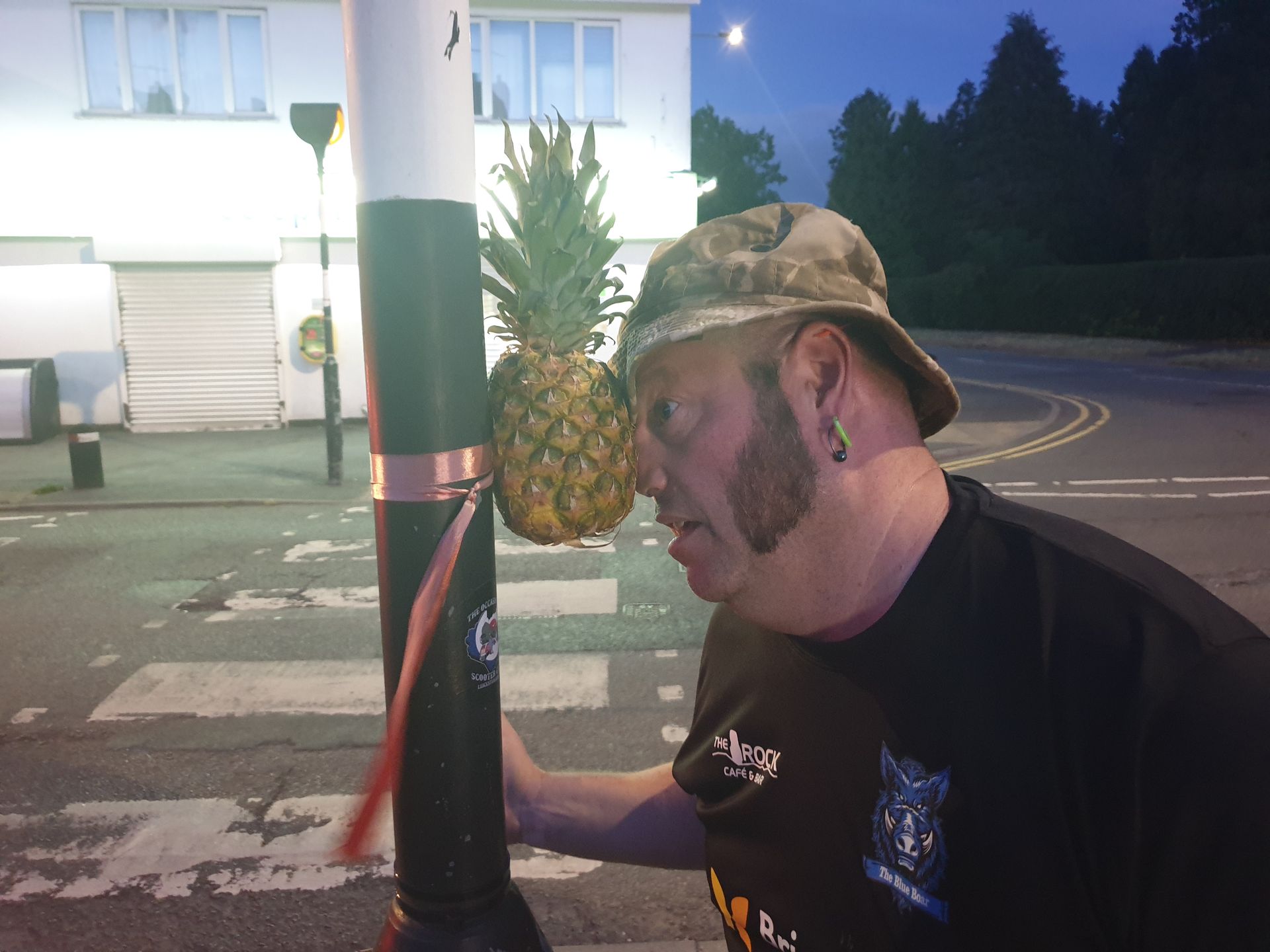 Man looking at pineapple attached to a street lamp at night.