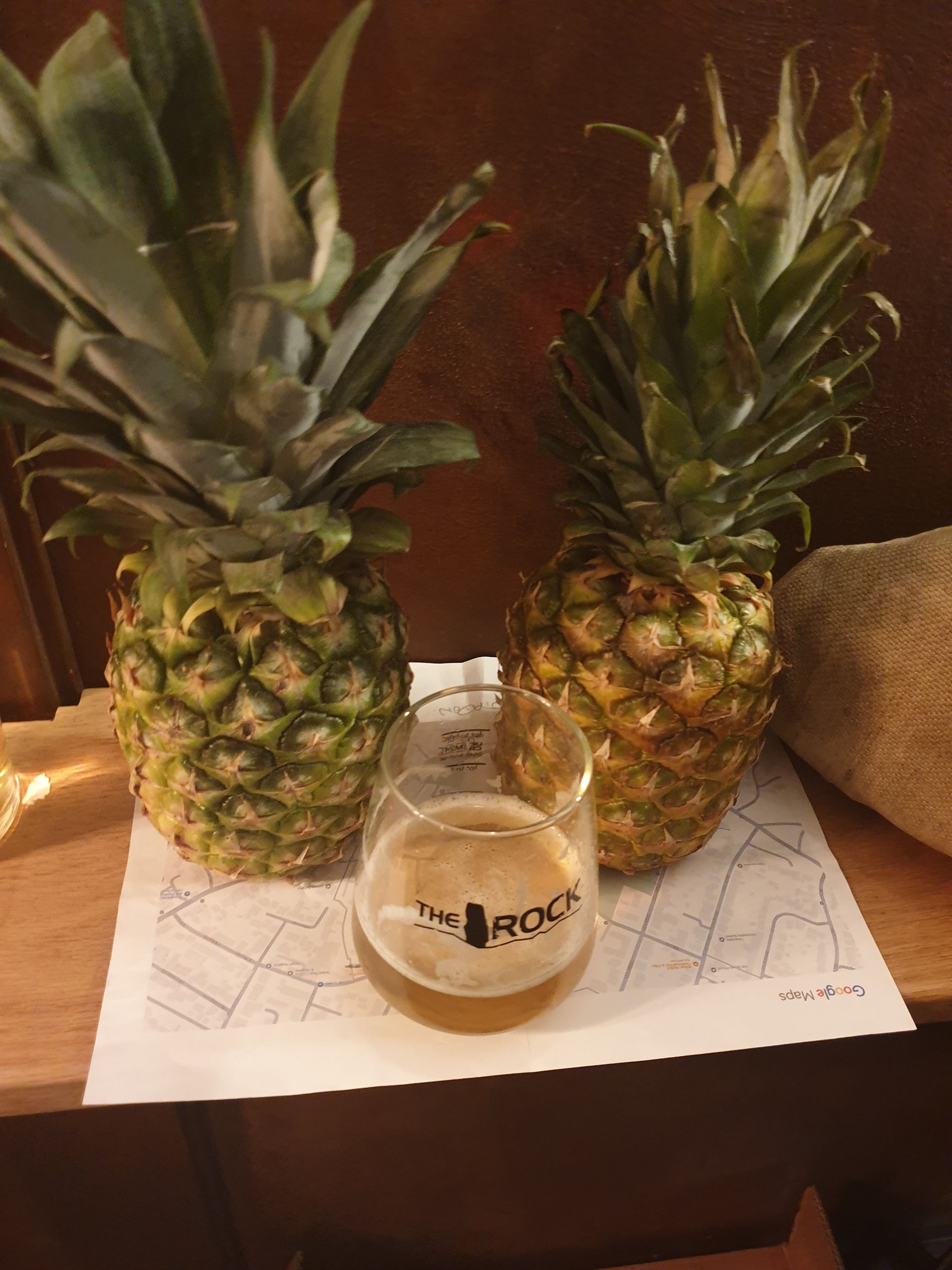 Two pineapples flank a beer glass, set on a map; wooden surface.
