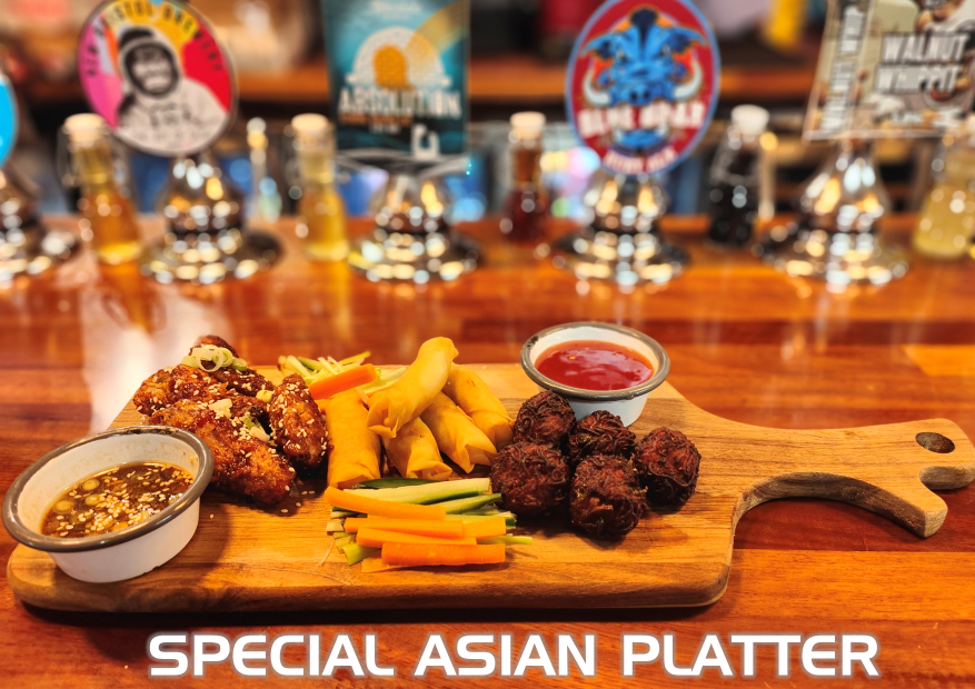 Asian appetizer platter on a wooden board: spring rolls, meatballs, wings, and dipping sauces.