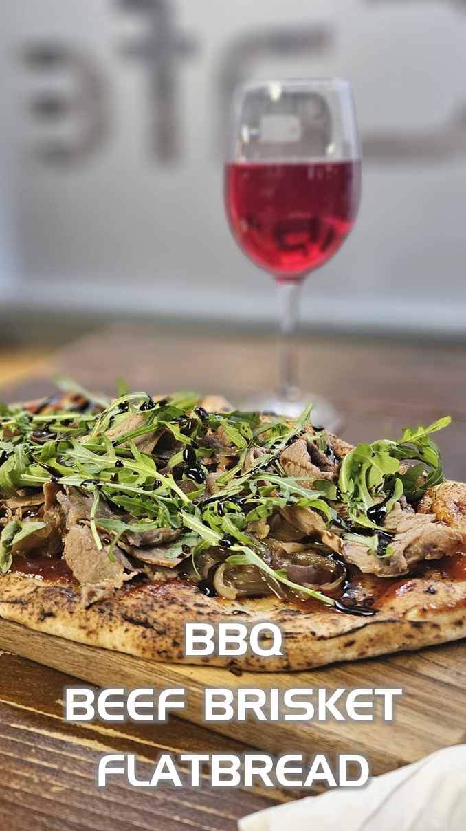 BBQ beef brisket flatbread topped with arugula and balsamic glaze, with a glass of red wine.