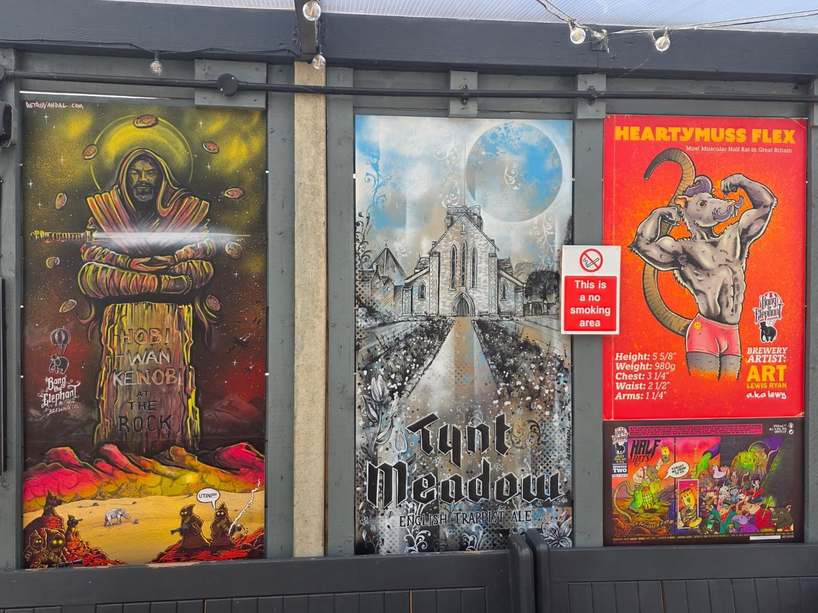 Three colorful posters on a wall. One with a haloed figure, one with a building and moon, and one with a flexing goat.