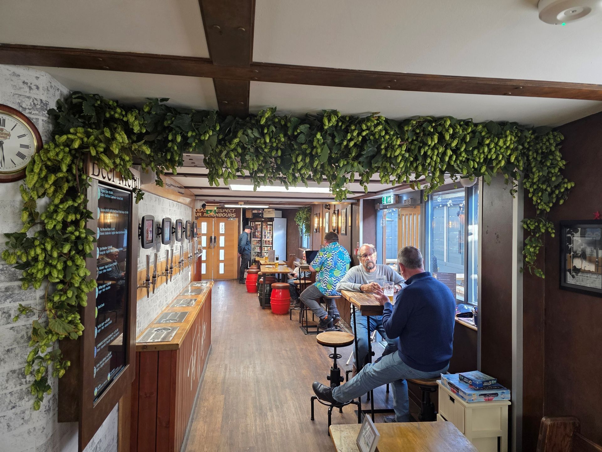 Interior of a pub with wooden beams and hop vines. People sit at tables, some drinking.