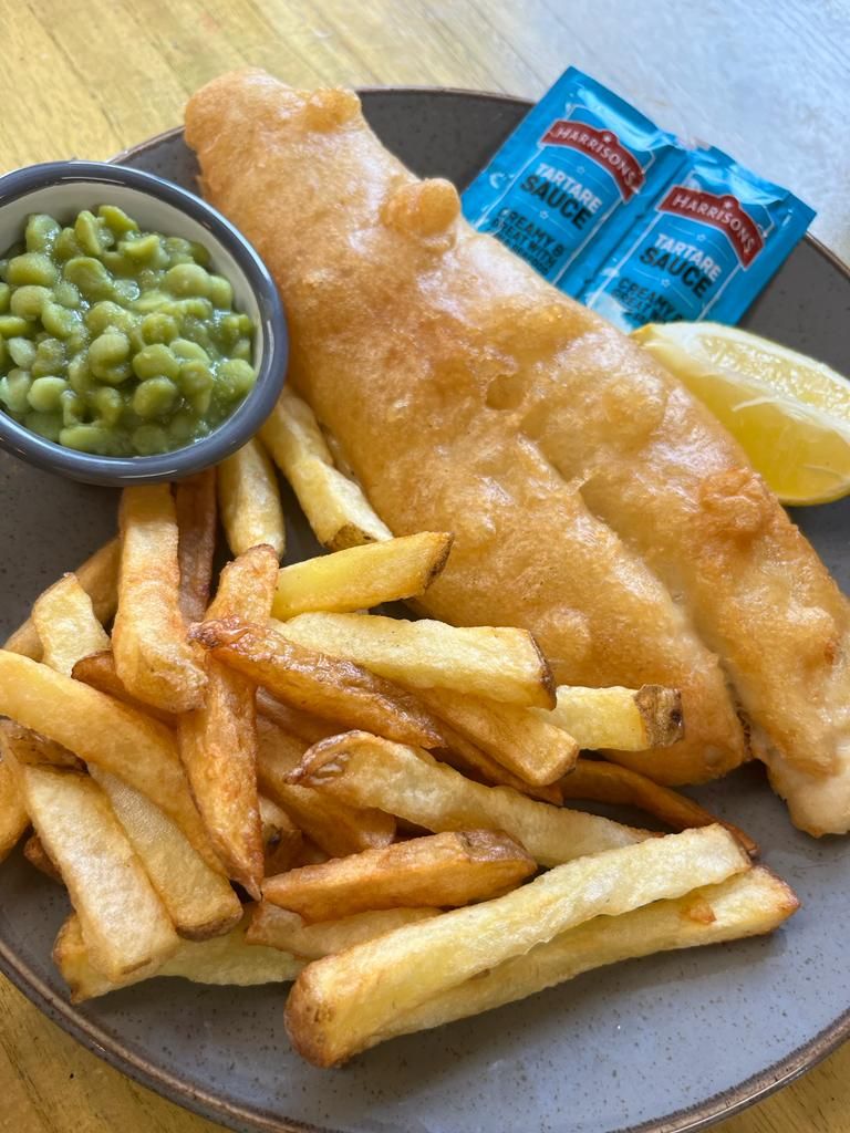 Fish and chips plate with mushy peas, tartar sauce, and lemon slice.