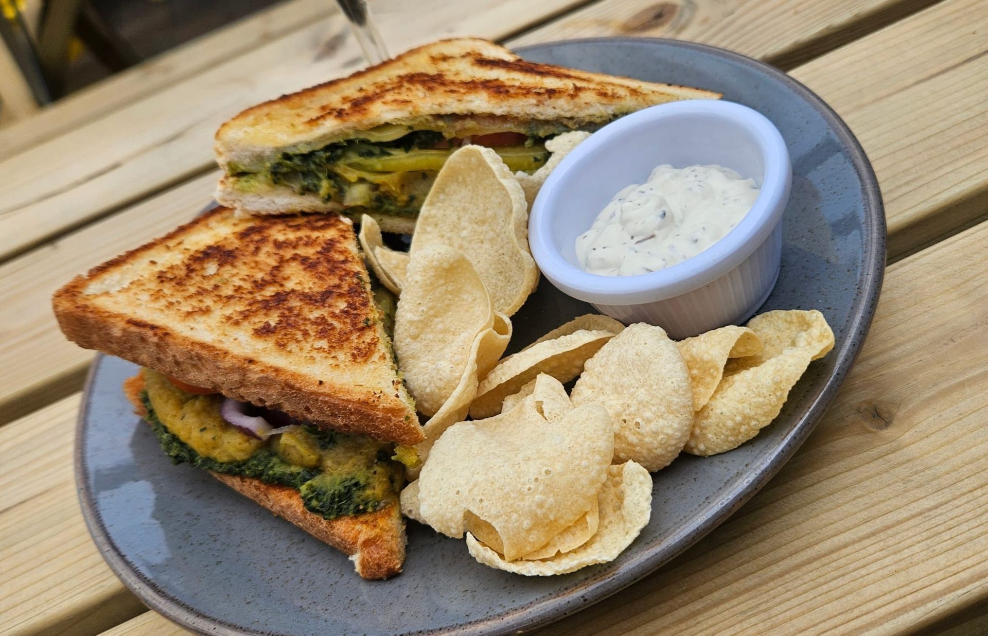 Grilled sandwich with chips and dip on a plate, set on a wooden table.