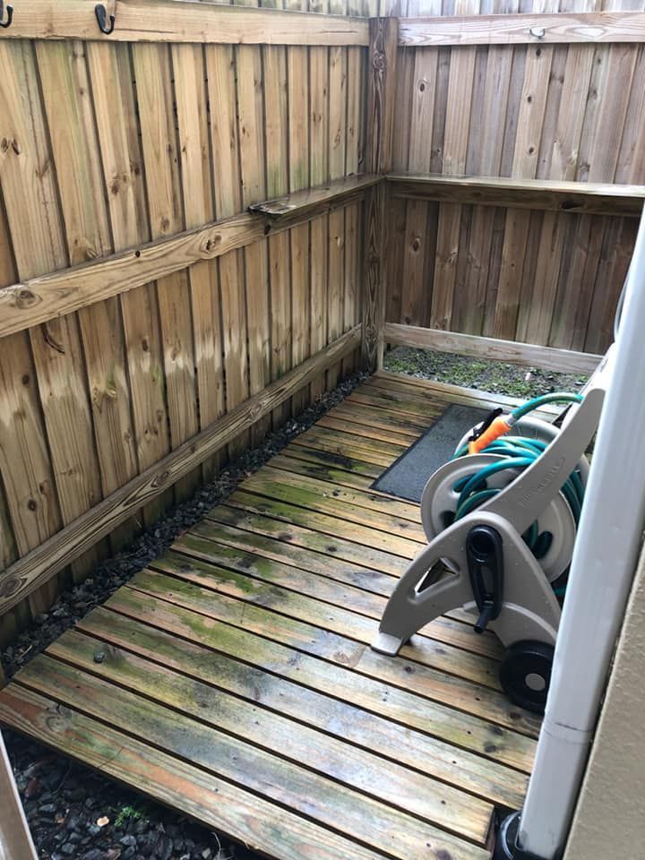 Wooden deck against a wooden fence, with a hose reel and some greenery visible.