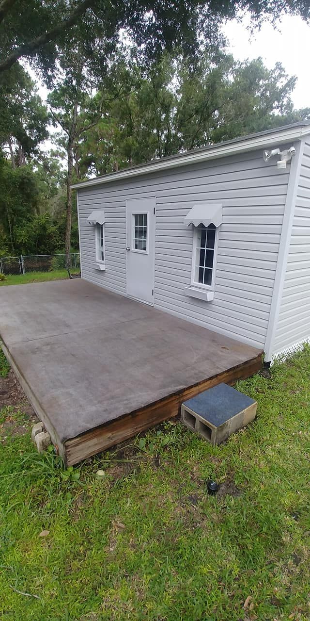 A small, white building with a wooden deck in a grassy yard.