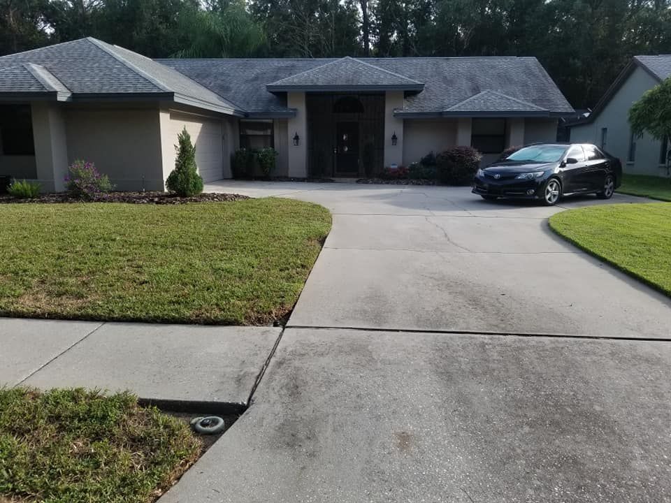 A black car parked in front of a light tan one-story house with a grey roof and well-manicured lawn.