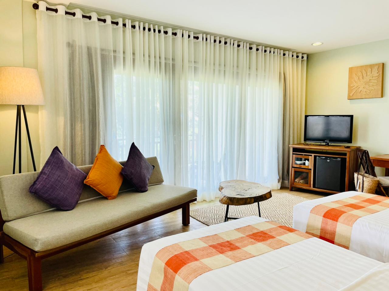 Bright bedroom with two beds, sofa, TV, and large sheer-curtained windows