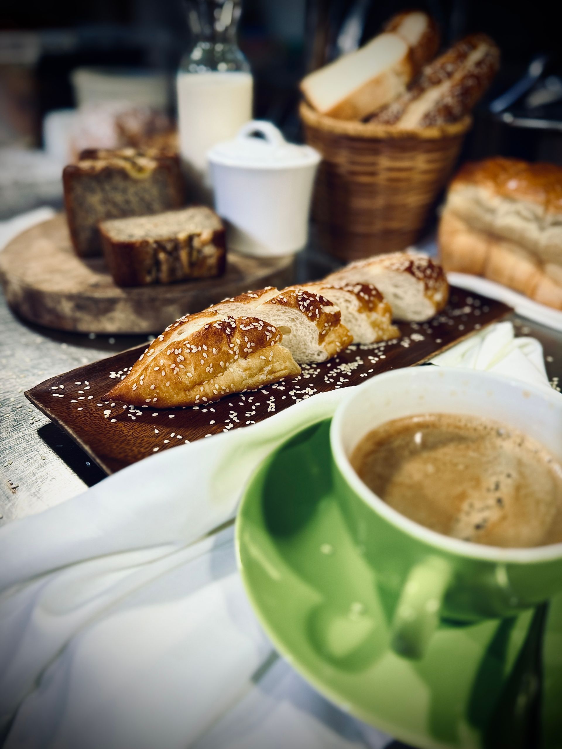 Coffee cup with pastry on a table, with baskets of bread and jars in the background