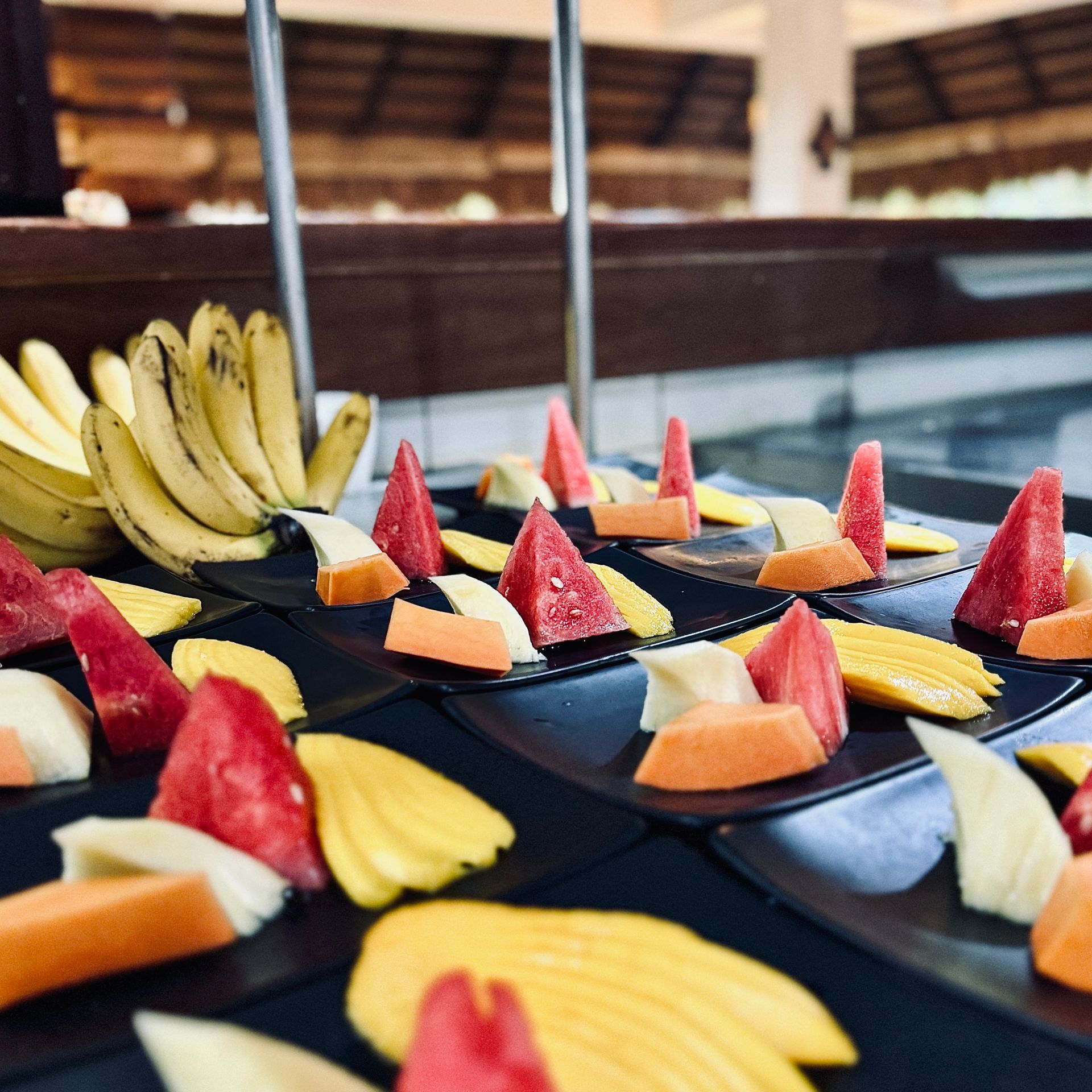 Fruit platter with watermelon, pineapple, banana, and melon slices arranged on black trays