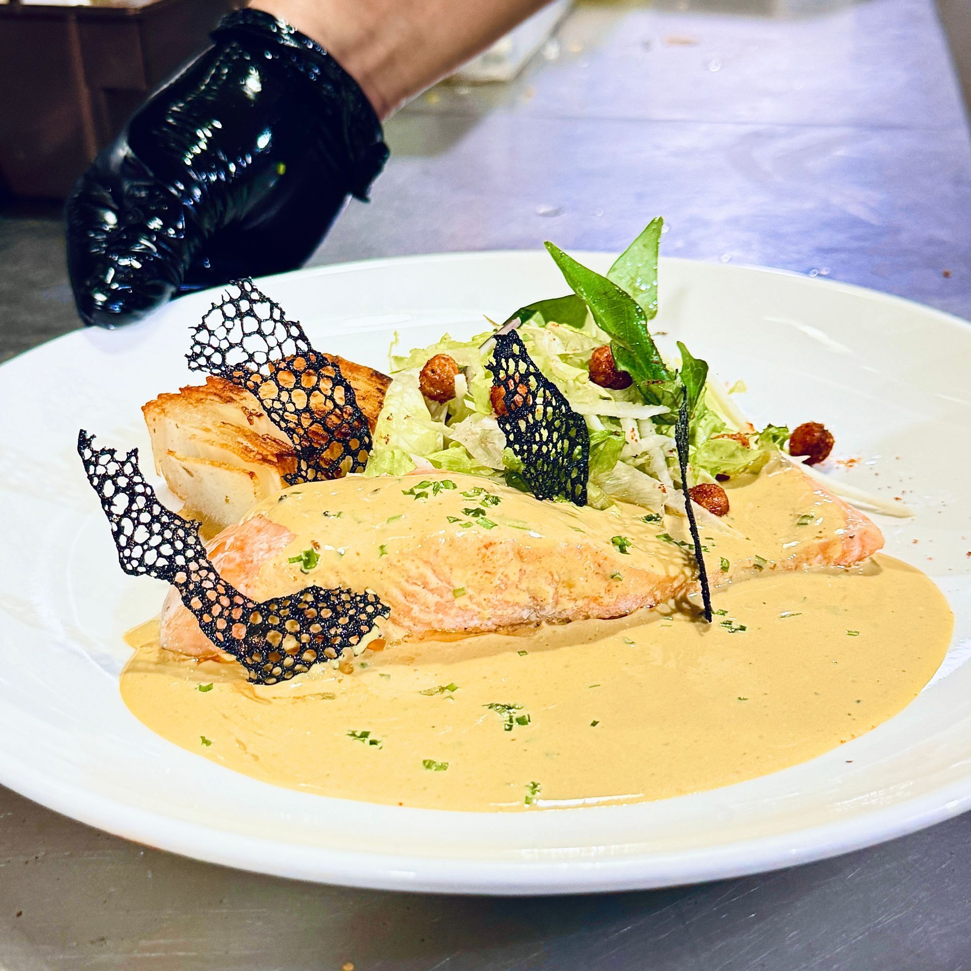 Plated salmon in creamy sauce with greens and black lace garnish on a white plate