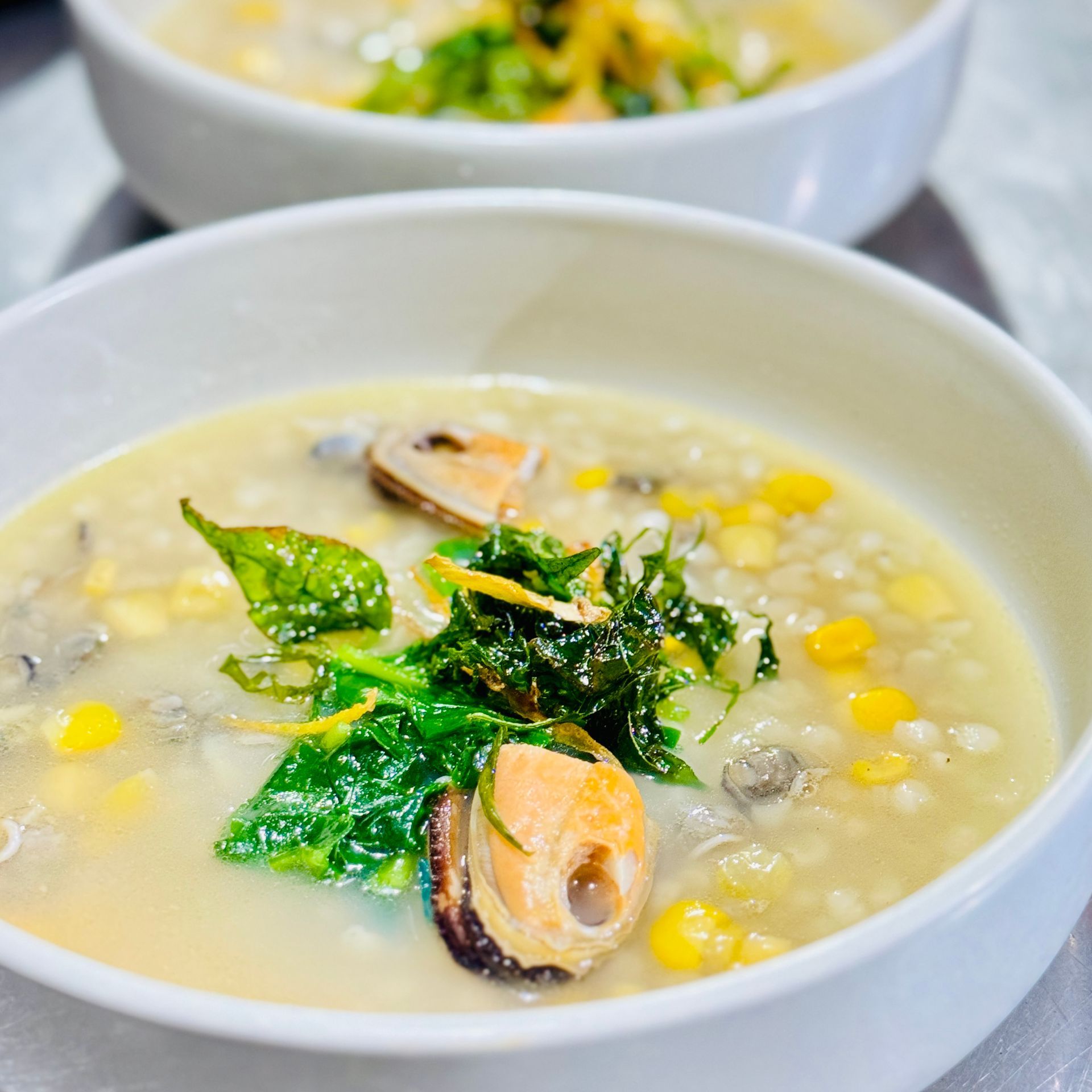 Two bowls of creamy soup topped with corn, greens, and sliced mushrooms