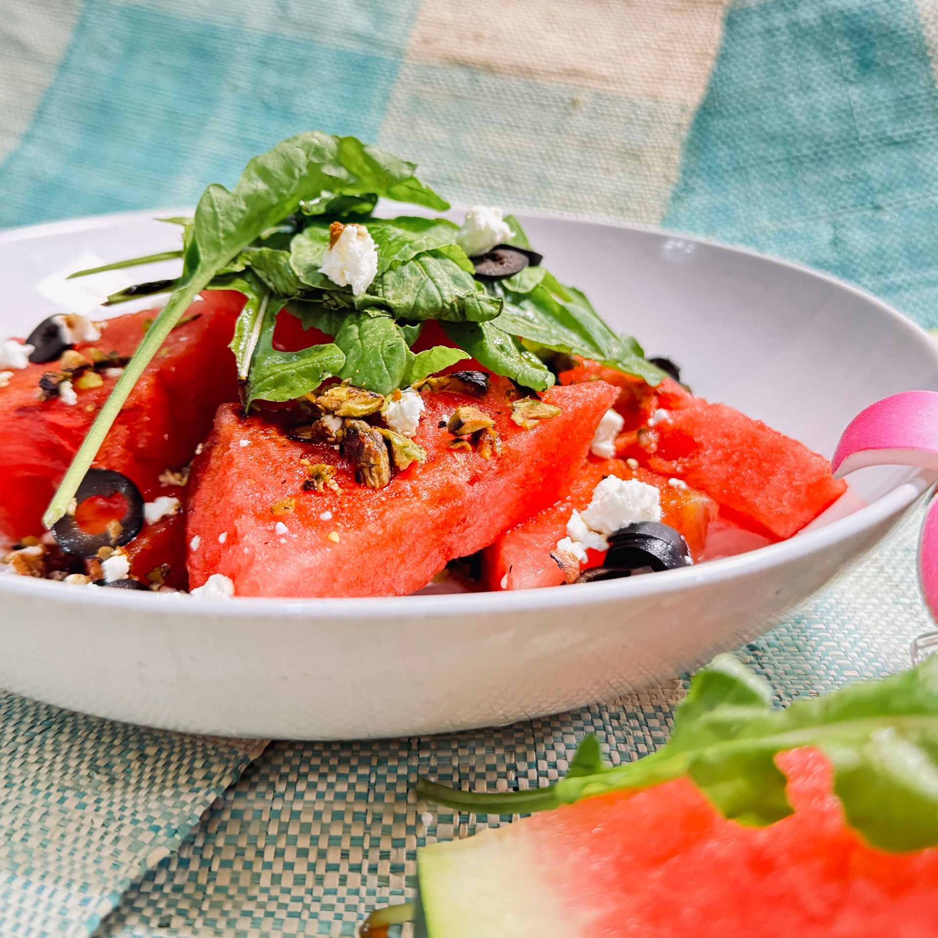 Watermelon salad with mint, berries, and cheese in a white bowl on a patterned tablecloth