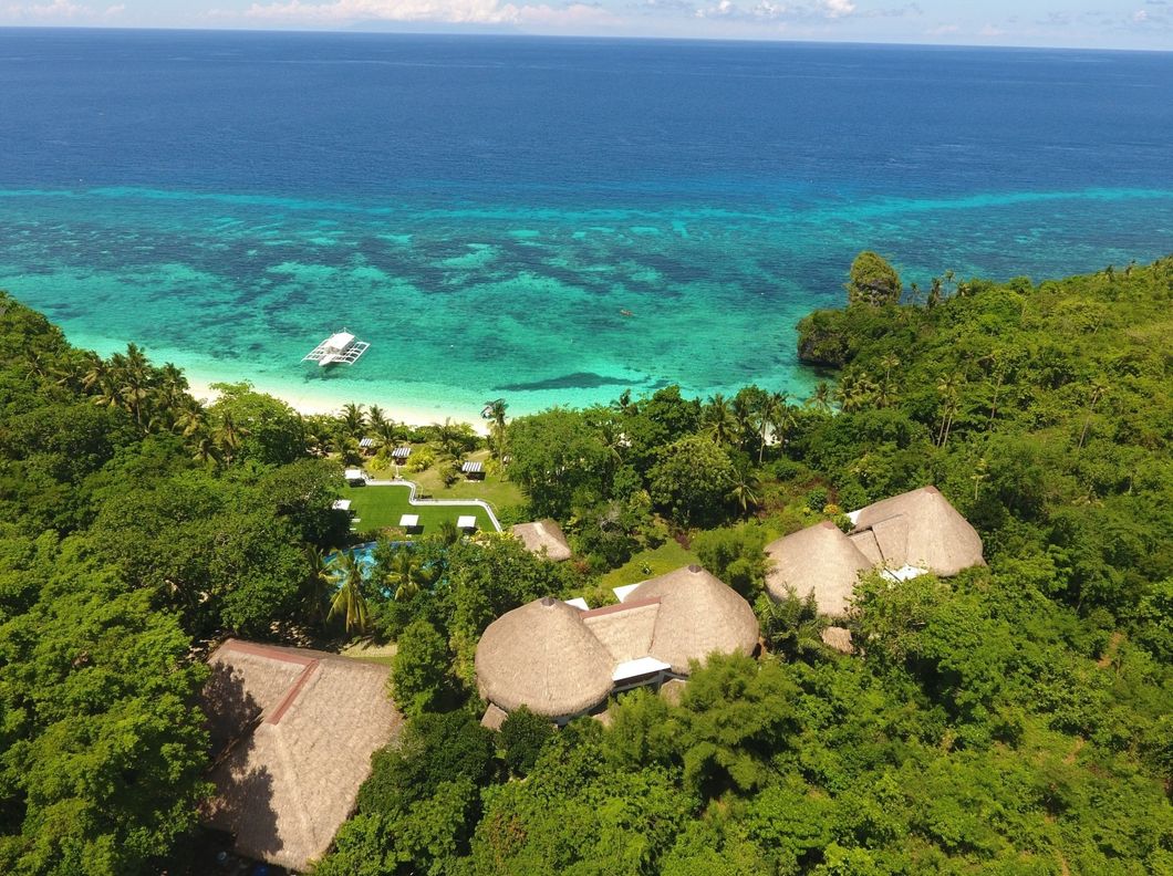 Tropical resort villas amid lush greenery overlooking a turquoise ocean with a small boat offshore