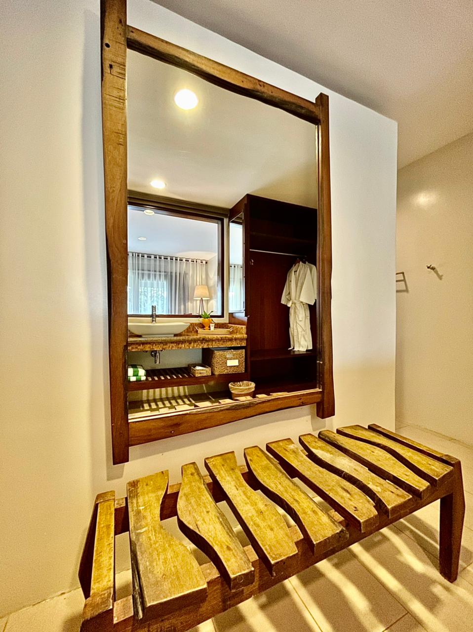 Wooden bench by a large wall mirror in a warmly lit room with a hanging robe.