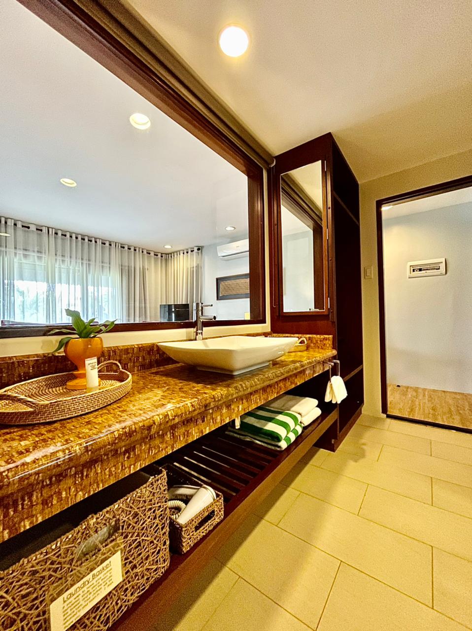 Hotel bathroom vanity with granite counter, large mirror, sink, and shelf stocked with rolled green towels.