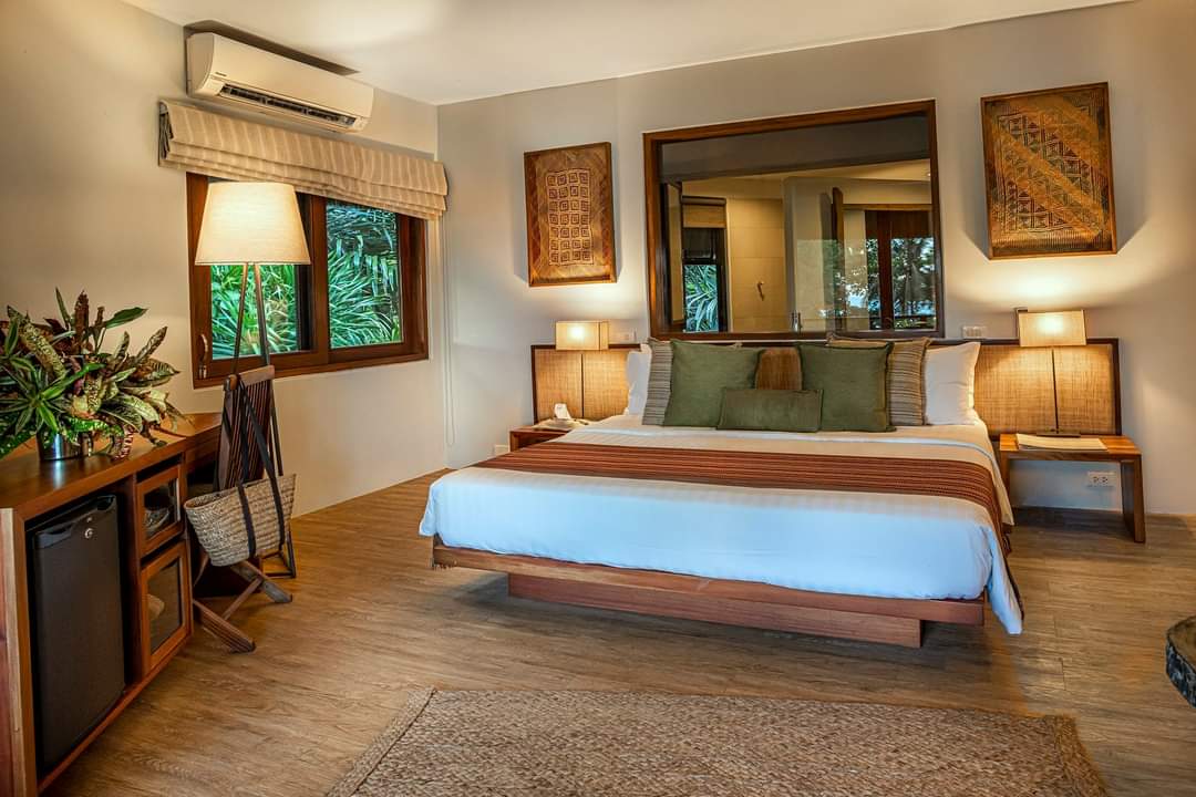 Cozy bedroom with a bed, wooden furniture, lamps, woven decor, and a window with green trees outside