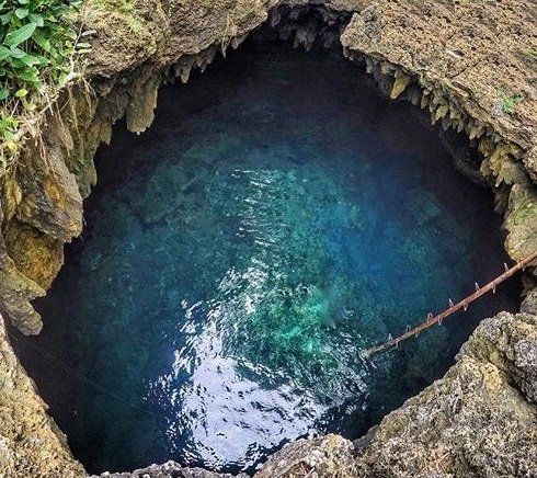 Rocky cave pool with clear blue water and a rope extending into it