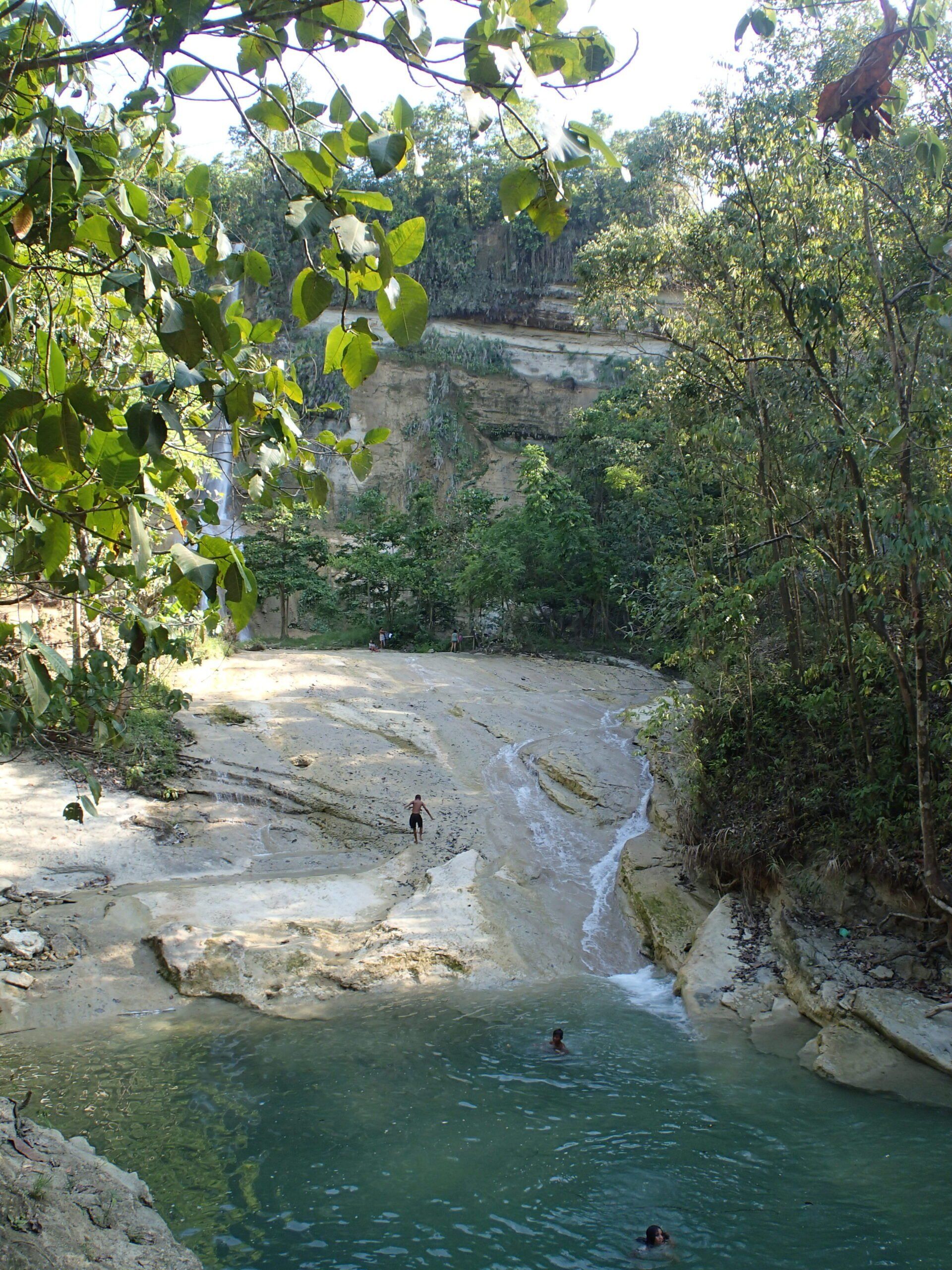 Small turquoise pool beside a rocky waterfall, surrounded by dense green foliage.