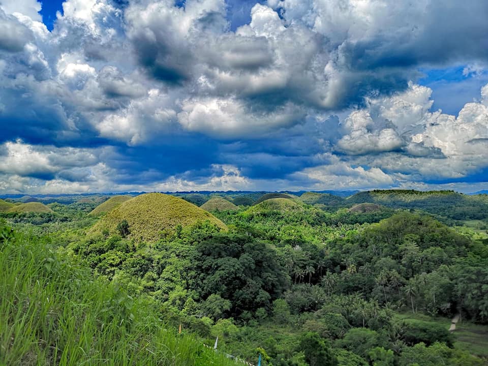 Lush green hills and forest under a dramatic blue sky with large white clouds