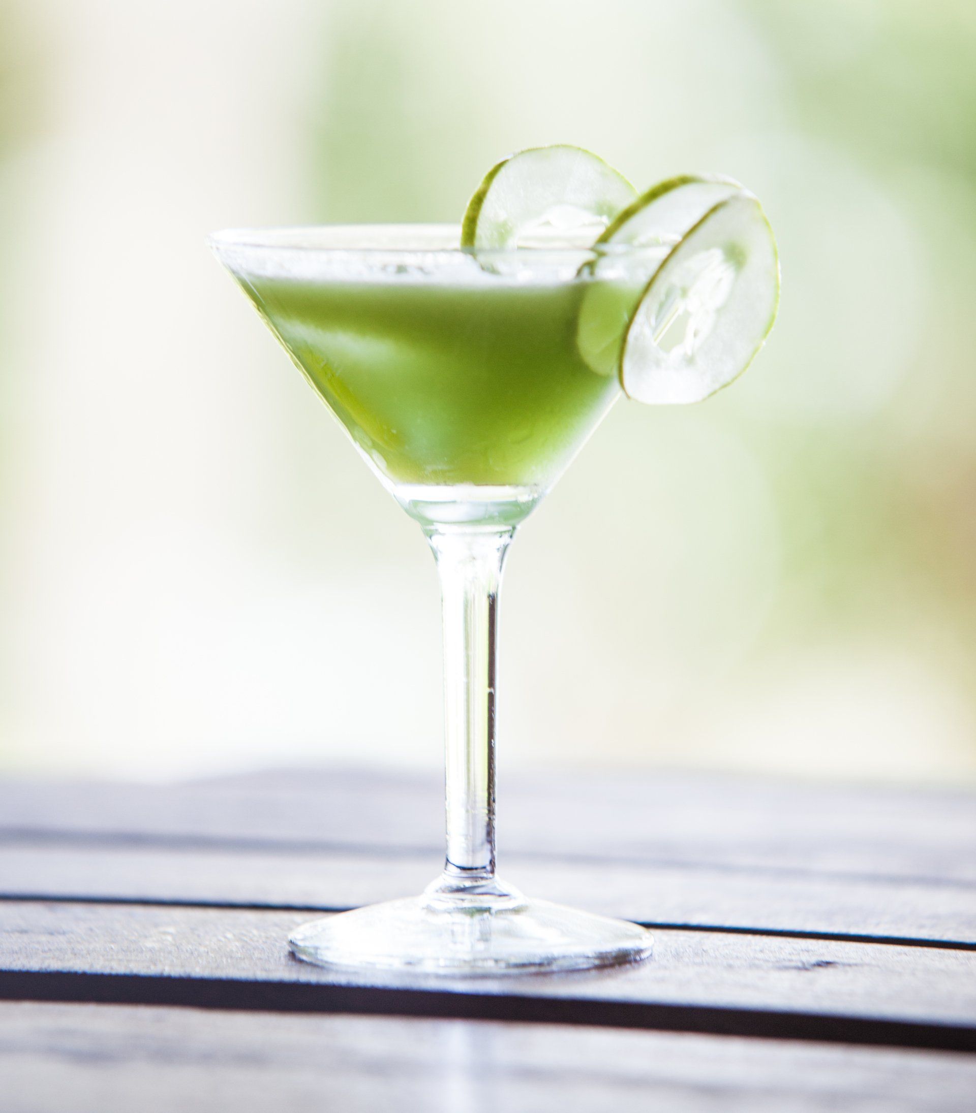 Green cocktail in a martini glass with lime slices on a wooden table