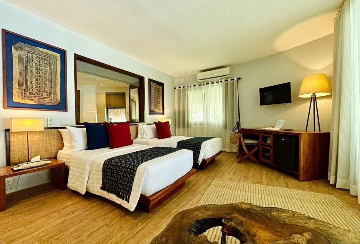 Cozy hotel room with a king bed, wall art, TV, lamp, and woven decor in warm neutral tones