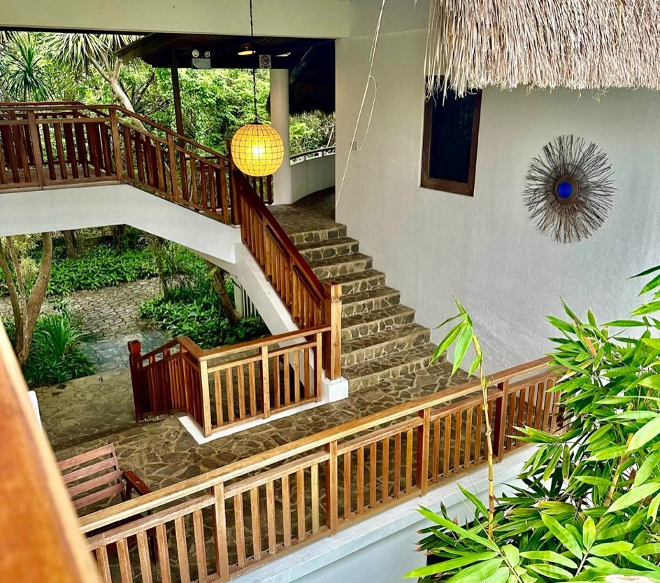 Wooden stairway and railings beside a white house, lit by a hanging lantern amid lush greenery.