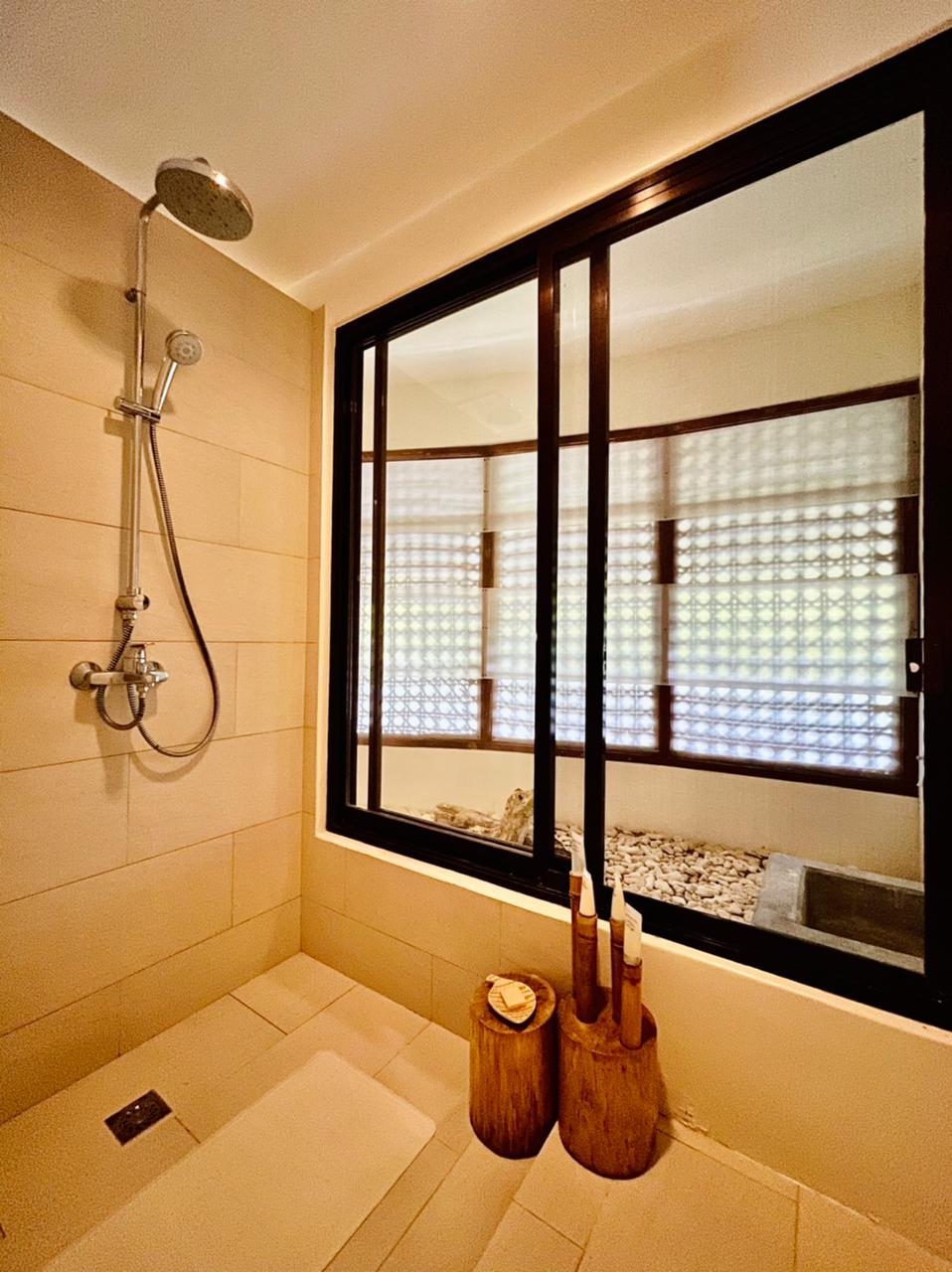 Modern bathroom with walk-in shower, glass window, and bath products on a tub ledge