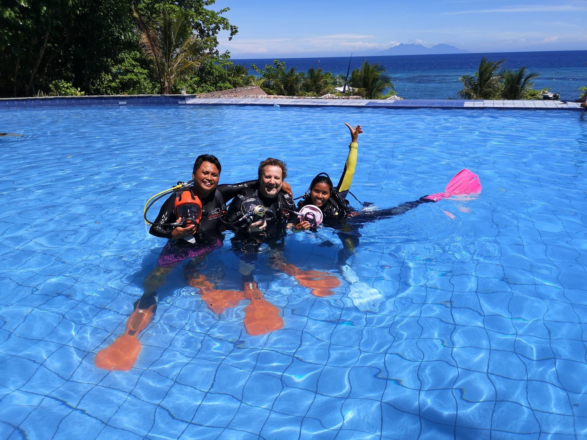 Introductory course in an infinity pool with ocean view, smiling and posing with fins raised