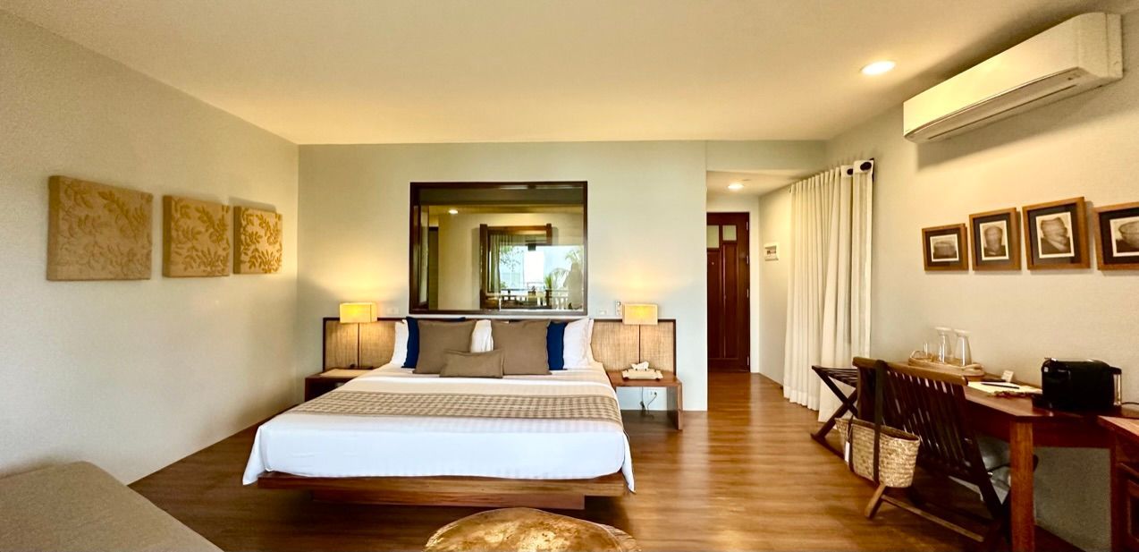 Modern bedroom with a large bed, warm wood floors, wall art, desk, mirror, and air conditioner