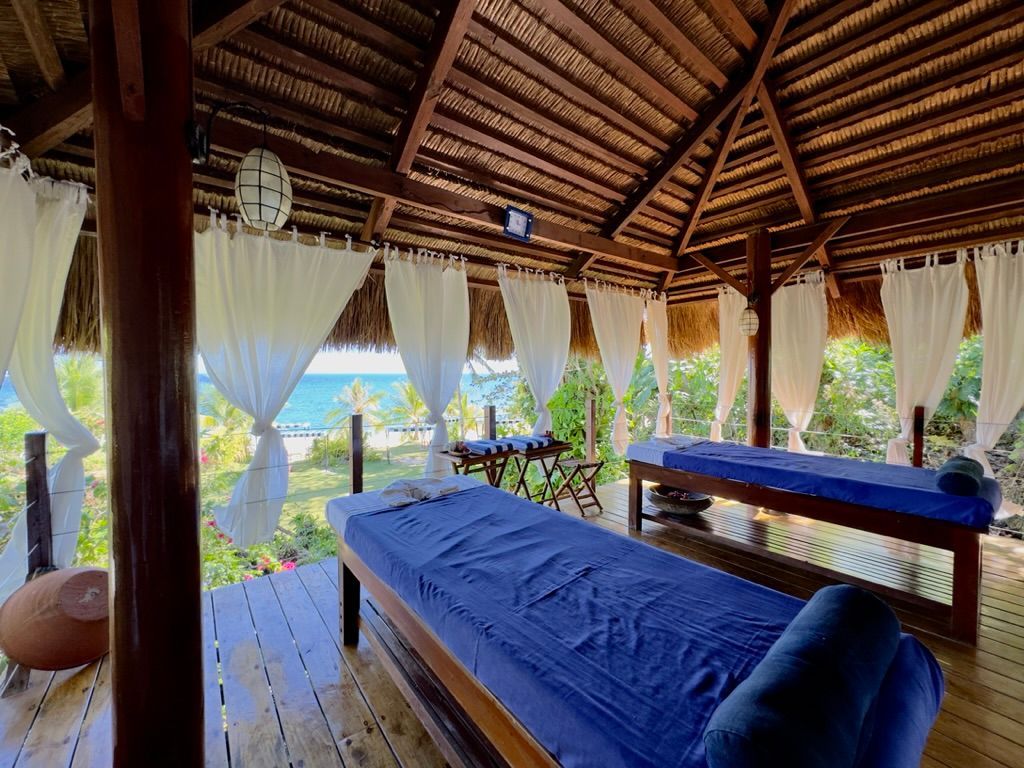 Open-air spa room with two massage beds, blue linens, and tropical ocean views