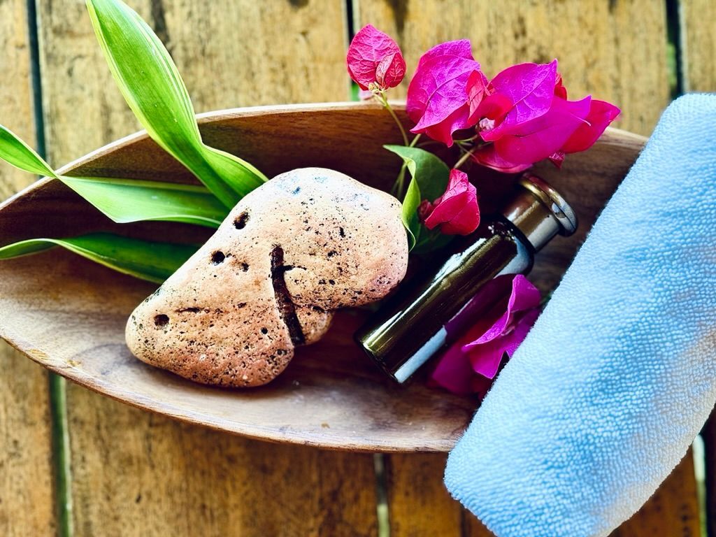 Spa items on a wooden tray with pink flowers, black bottles, a stone, and a blue towel