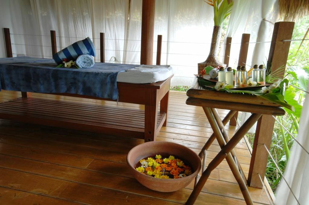 Cozy porch with wooden bed, small table of bottled drinks, and a bowl of fruit on the floor