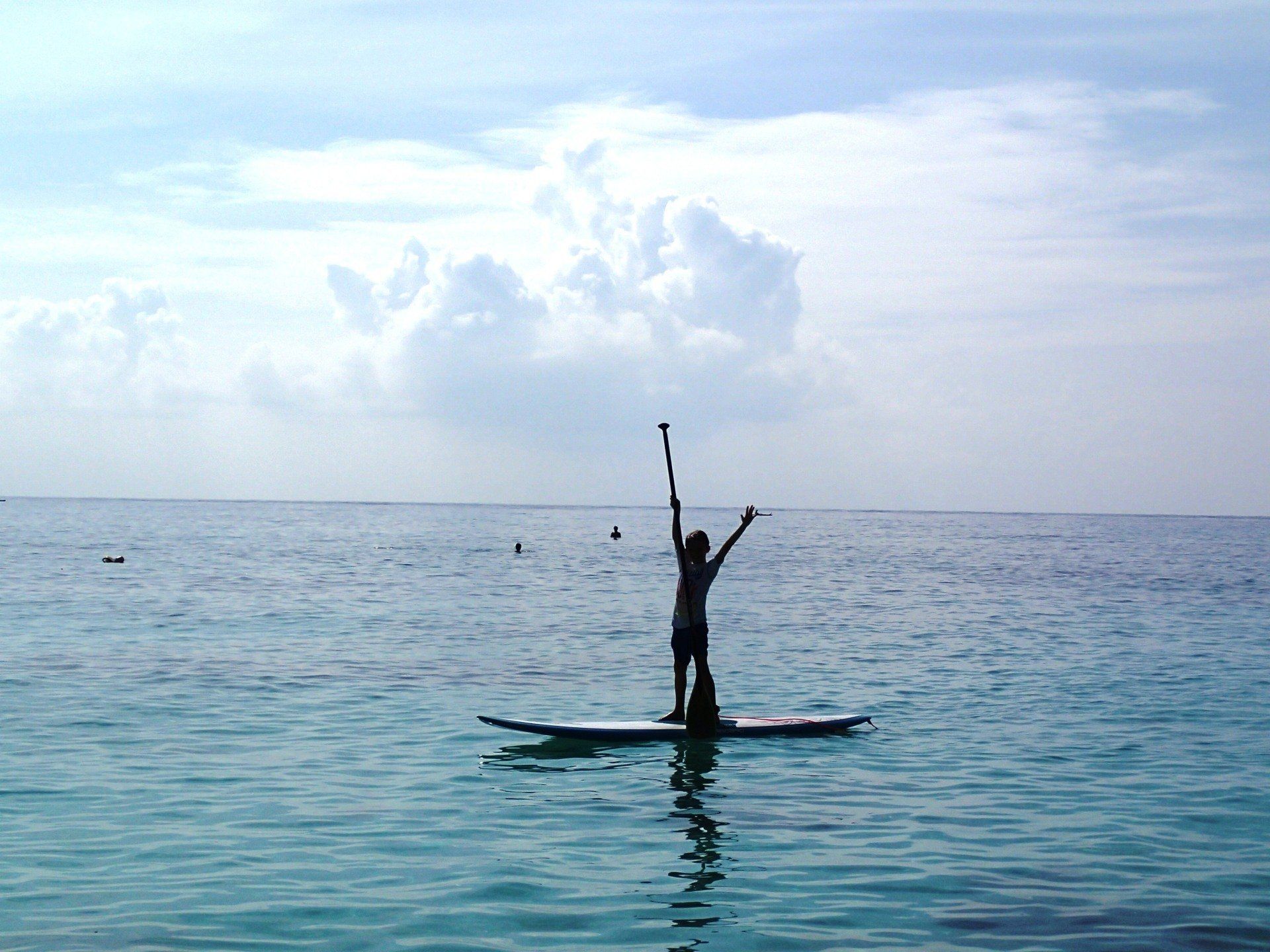 Person standing on a paddleboard on calm blue ocean under a cloudy sky