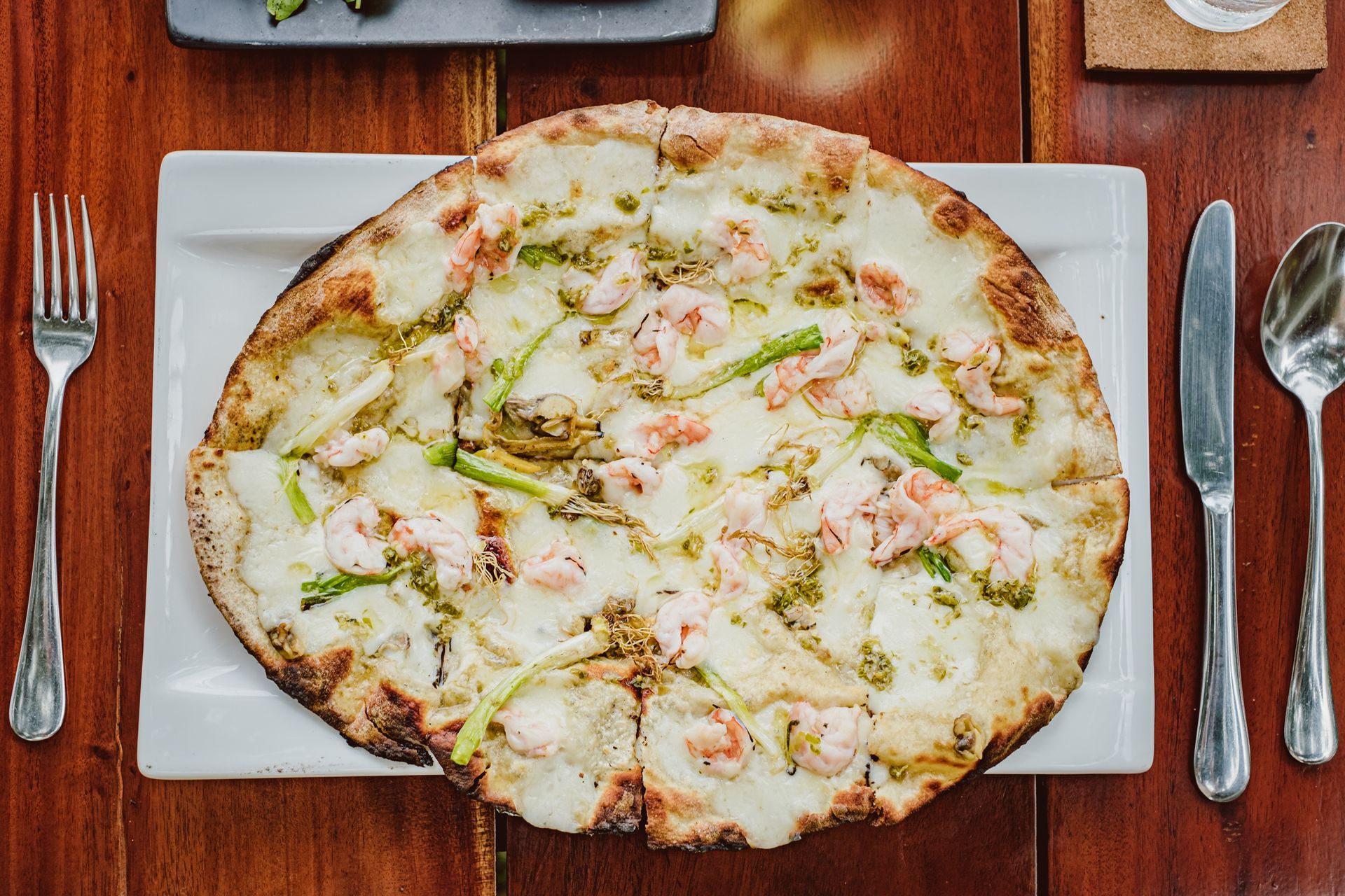 Pizza on a white plate with silverware on a wooden table