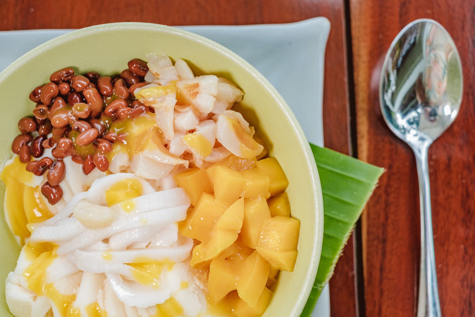 Fruit and bean dessert in a green bowl with a spoon on a white plate